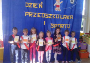 Grupka dzieci w czerwonych szarfach pozuje do zdjęcia trzymając przed sobą dyplomy.
